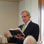 A man is reading from a book in one hand and gesturing with his other hand